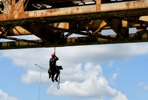 Przewodnik z psem służbowym wisi na linie na moście