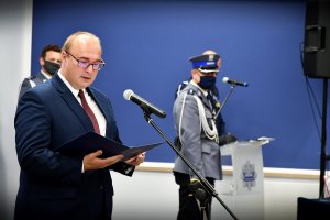 Mężczyzna przed mikrofonem. W oddali policjant.