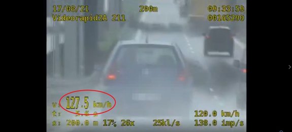 Samochód na pasie ruchu i dane dotyczące pomiaru prędkości. W czerwonym kole zaznaczona jest wartość 127,5 km/h