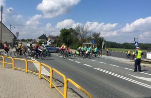 Policjant ruchu drogowego zatrzymał ruch pojazdów na ulicy Kluczborskiej w Wojciechowie. Przed nim przejeżdżają rowerzyści. W tle widoczny postawiony w poprzek oznakowany radiowóz i drugi policjant.