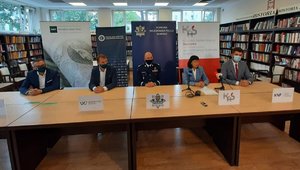 komendant wojewódzki siedzi obok innych osób przy stole prezydialnym podczas konferencji prasowej, na stole poustawiane mikrofony