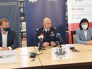 komendant wojewódzki siedzi obok innych osób przy stole prezydialnym podczas konferencji prasowej, na stole poustawiane mikrofony
