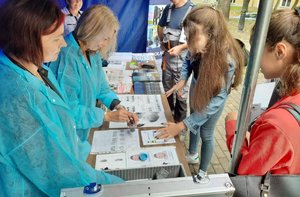 2 kobiety w fartuchu przy stoisku do pobierania linii papilarnych, naprzeciwko stoją 2 dziewczynki