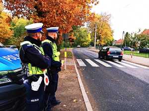 dwóch policjantów stoi przy radiowozie obok drogi