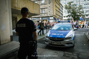 policjanci stoją na chodniku obok idzie marsz