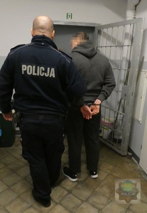 Umundurowany policjant prowadzi zatrzymanego mężczyznę.