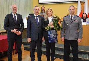 uczestnicy konferencji stoją obok siebie, kobieta trzyma w dłoniach kwiaty