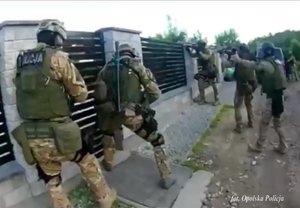 policjanci realizujący zatrzymanie - funkcjonariusze w moro przy bramie posesji i przy posesji