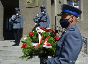 policjant z wieńcem w dłonie, w tle 2 policjantów przed tablicą pamiątkową