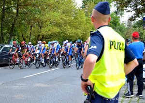 policjant stoi na chodniku, ulicą jedzie peleton