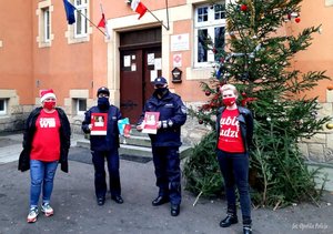 policjanci wręczają paczki przedstawicielom akcji szlachetna paczka. w tle choinka