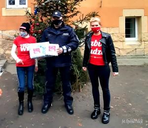 policjanci wręczają paczki przedstawicielom akcji szlachetna paczka. w tle choinka