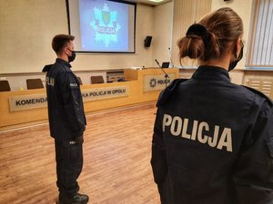 dwóch policjantów odwróconych plecami, w tle napis i logo KWP w Opolu