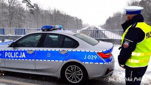 policjant stoi przy radiowozie  i patrzy w kierunku autostrady