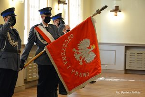 3 policjantów 1 ze sztandarem stoi obok siebie