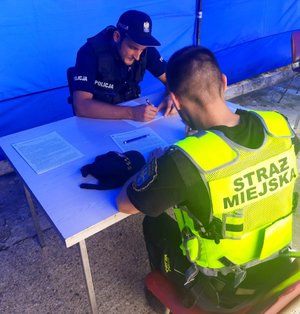 policjant i strażnik miejski przy stole wypełniają dokumenty