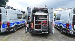 trzy radiowozy stoją obok siebie. Mają otwarte drzwi tylne wewnątrz widać rożny sprzęt wykorzystywany przez policjantów